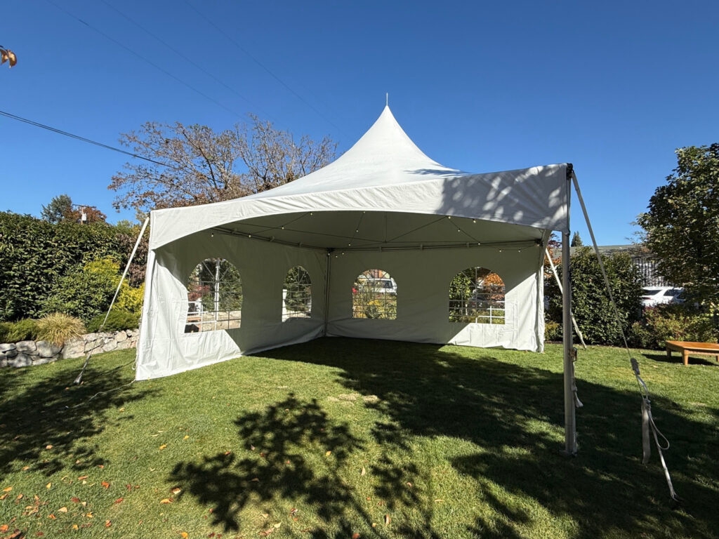 White high-peak tent on grass with arched window sidewalls, an open front and string lights beneath the canopy.