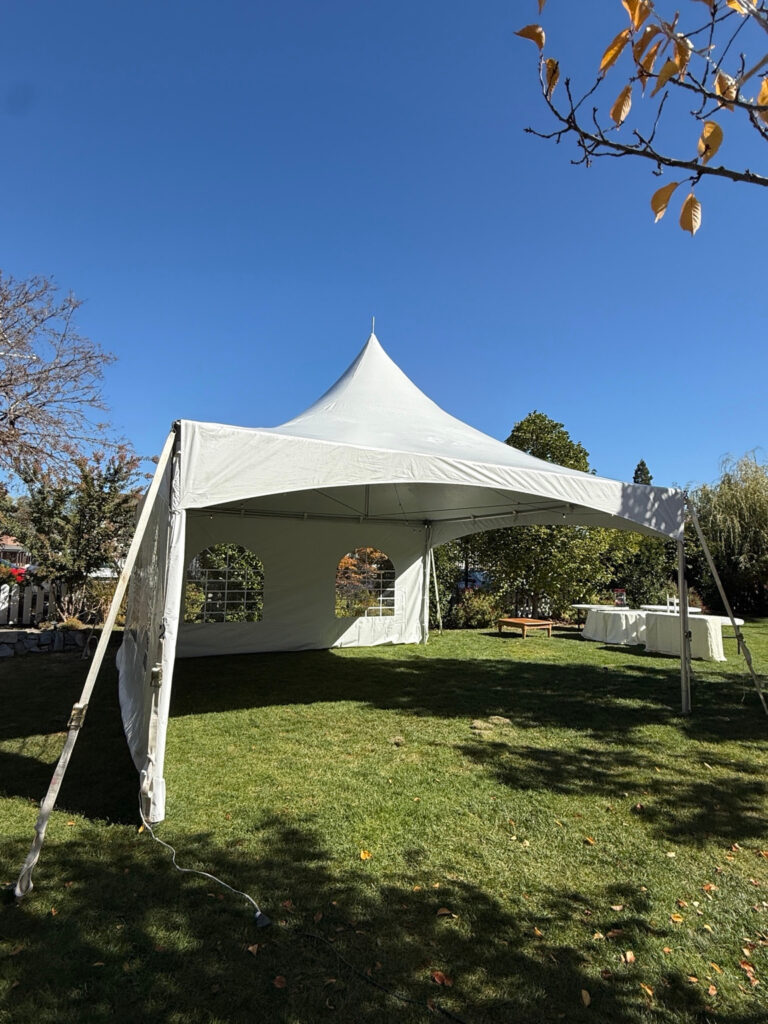 Angled view of a white high-peak tent on grass with arched window sidewalls and an open front.